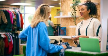 A customer speaks with a smiling employee at the checkout counter of a clothing pop-up shop.