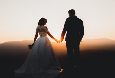 A man in a suit and a woman in a white wedding dress are standing together while they are holding hands.