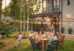 A family gathered together in the backyard of a large house. Kids are running around while adults are sitting.