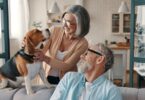 An older couple smiles and spends time with their beagle while relaxing together in their bright, modern home.