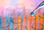 A close-up of a collection of small lab test tubes with a dropper of liquid hovering over one test tube.