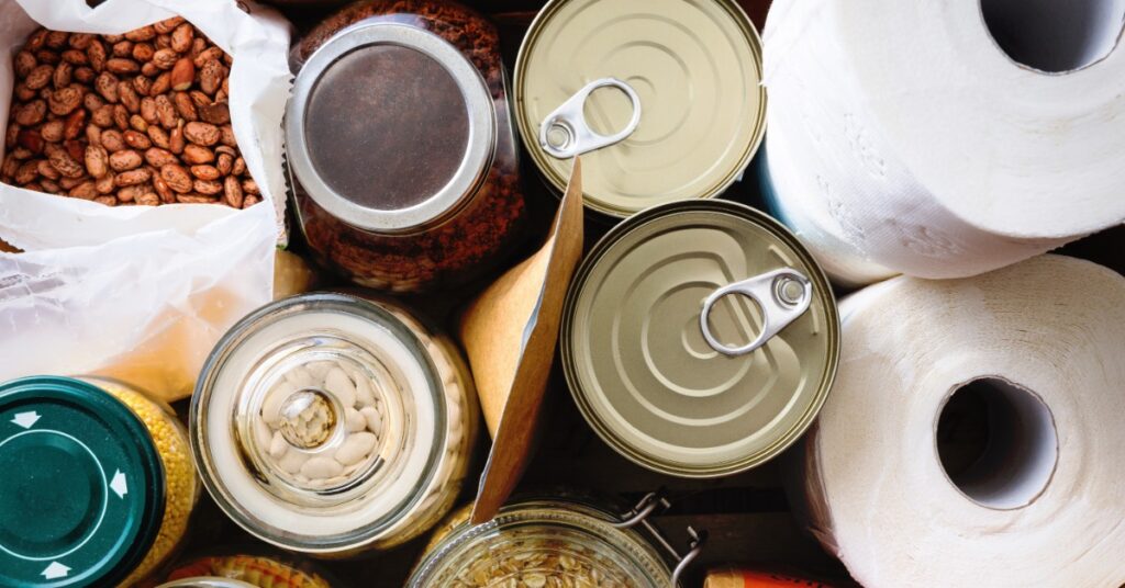 Assorted pantry supplies include canned goods, jars of beans and oats, dried beans, paper towels, and packaged food.